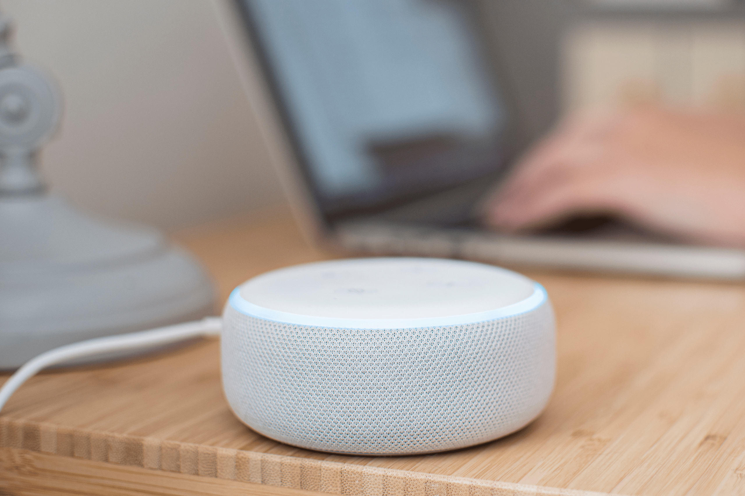 A white Alexa Smart Device sits on a wooden desk