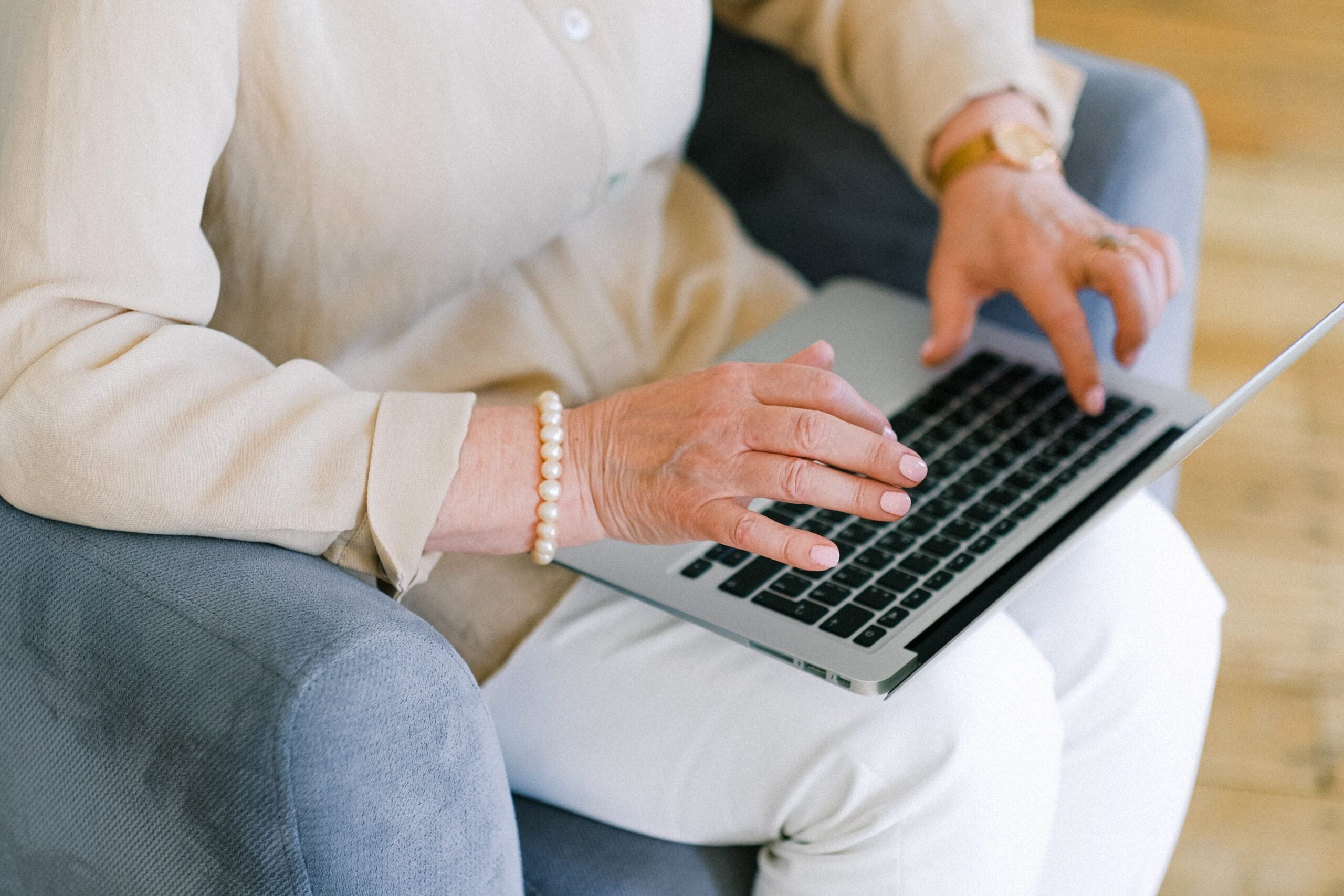 Female senior citizen using laptop. The laptop is in her lap as she uses the computer to make searches.