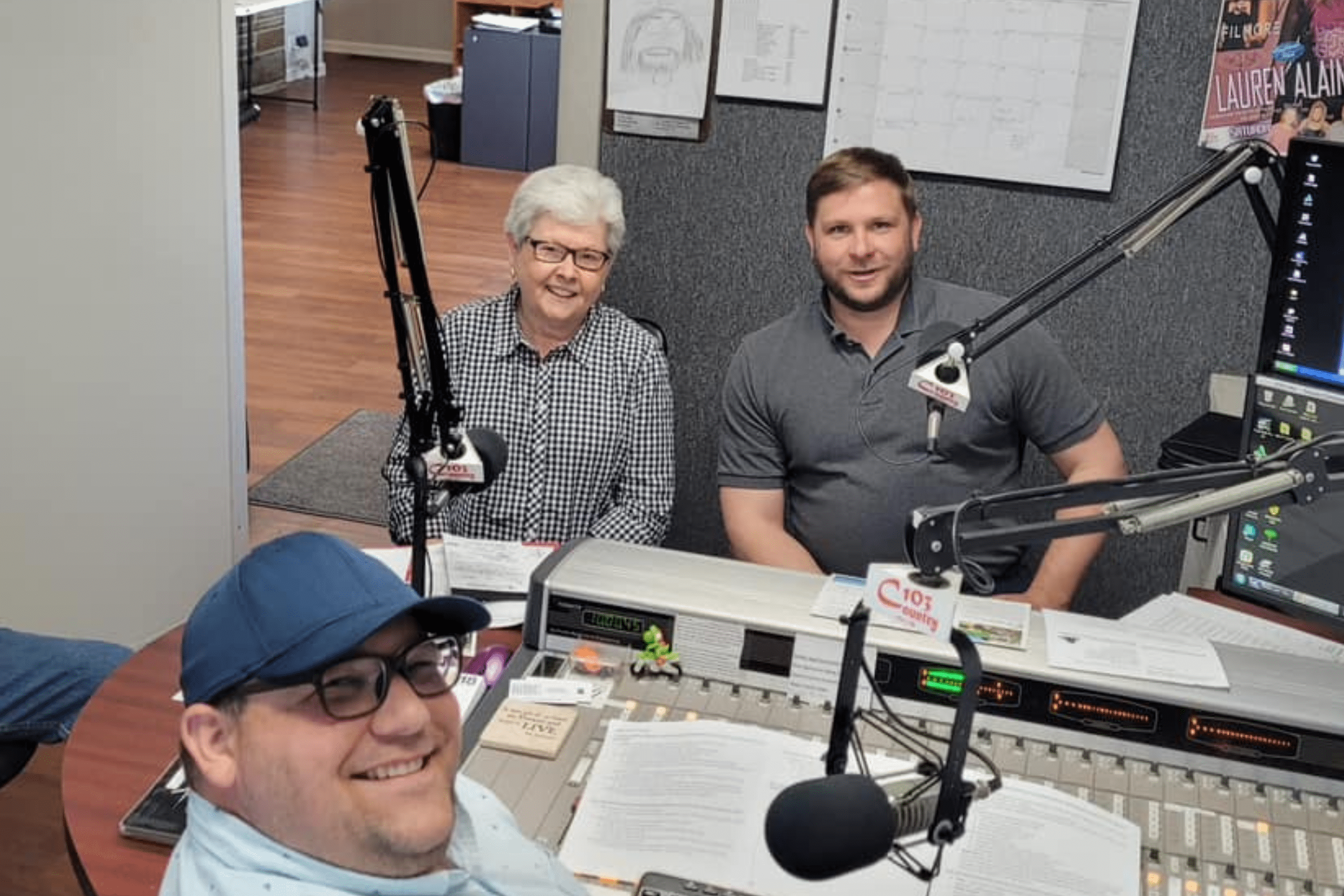 Image of board members Linda Stepp and President Paul Worley engaged in conversation with host Matt Hilderbrand during an interview on C103. They are seated in a radio studio setting, gesturing and sharing insights about the organization's mission and community-focused initiatives.